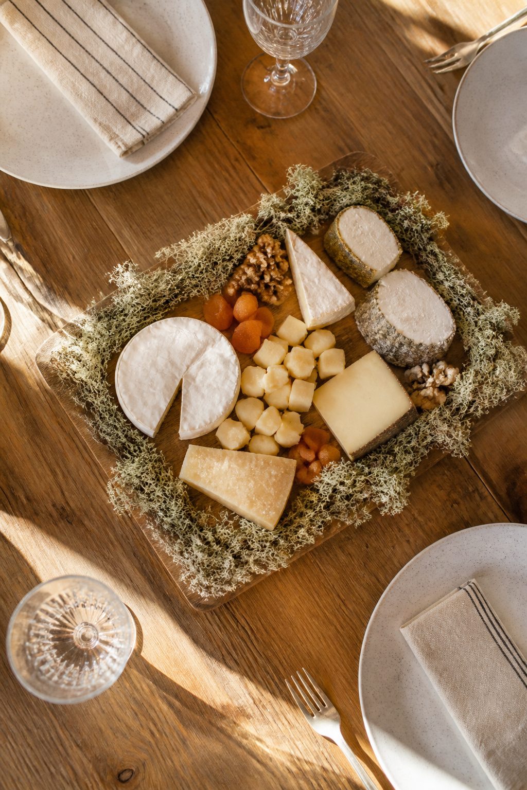 Wooden serving board edged with moss holding cheese.