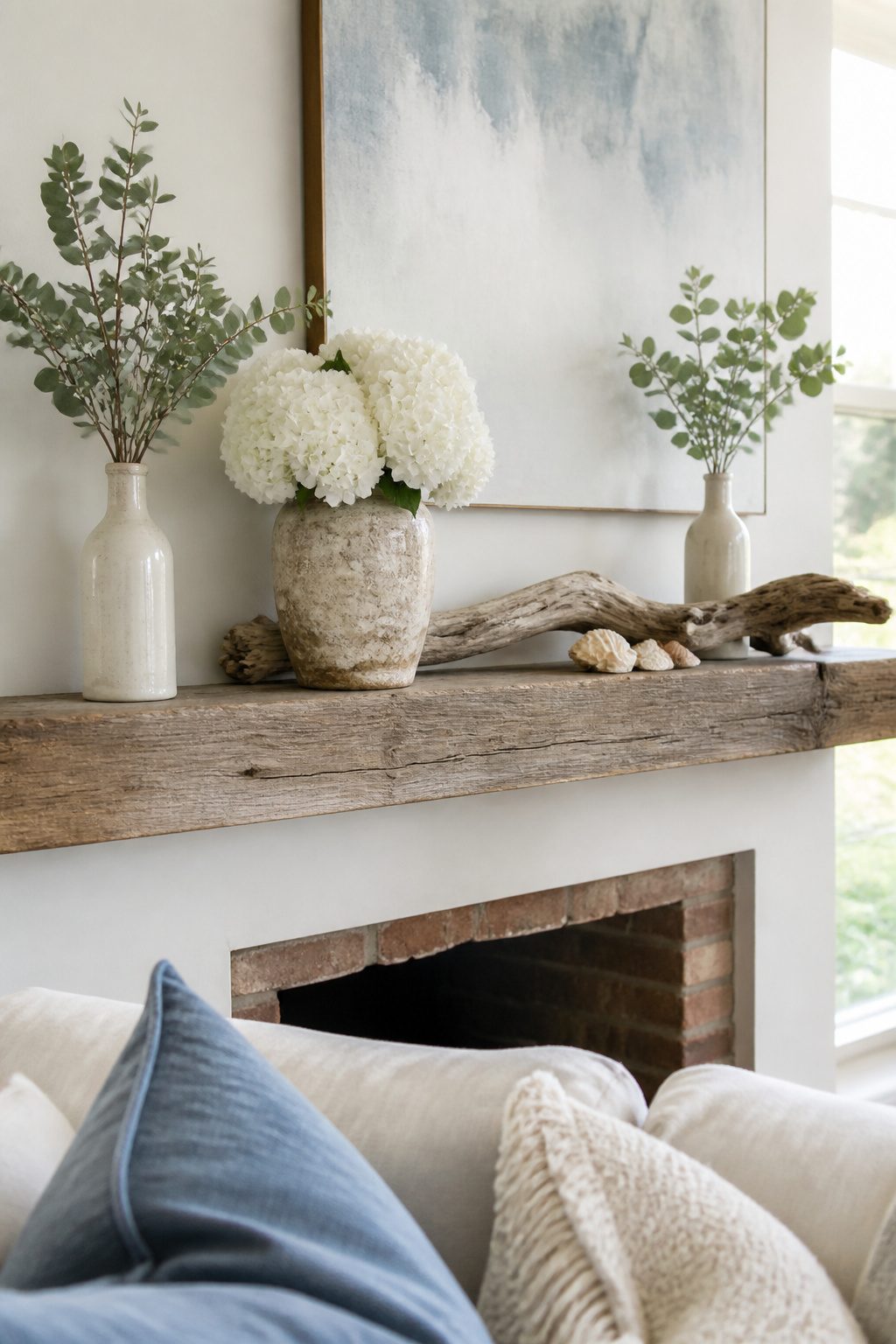 A mantel with white hydrangeas, eucalyptus branches, and seashells.